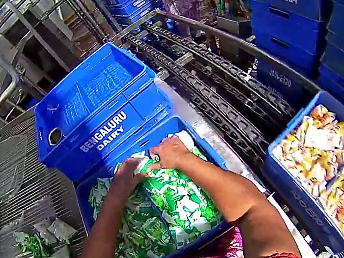 Sorting packed goods between crates beside a production line.