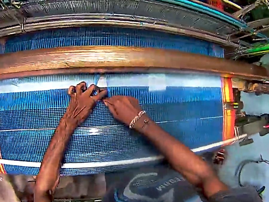 Hands working the warp threads across the width of a handloom.